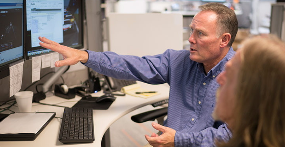 Two people sitting in front of a computer talking about what is on the screen