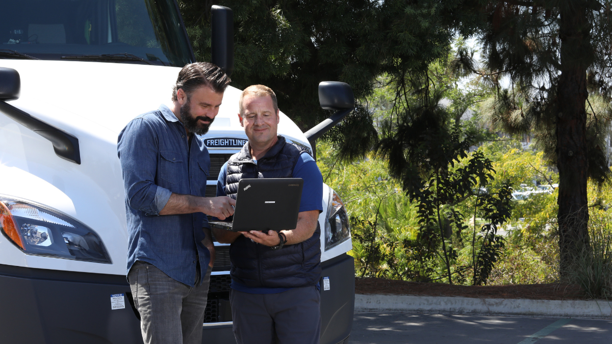 2 men looking at a laptop in front of a truck