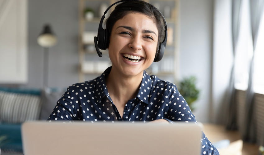 person smiling with a headset on in front of a laptop