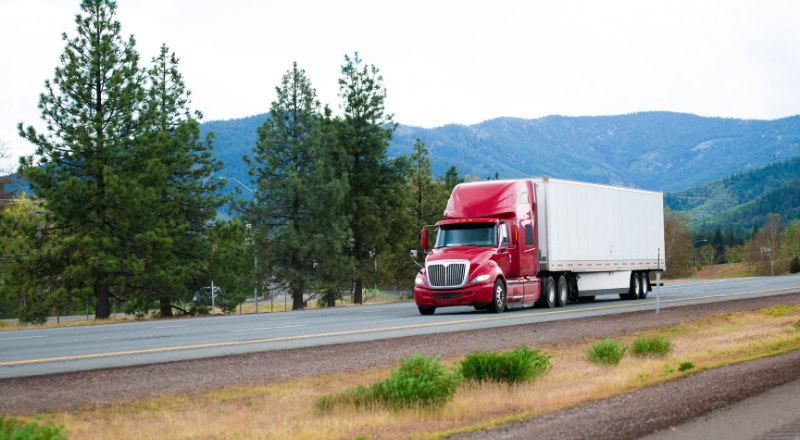 red semi truck driving down a rural road