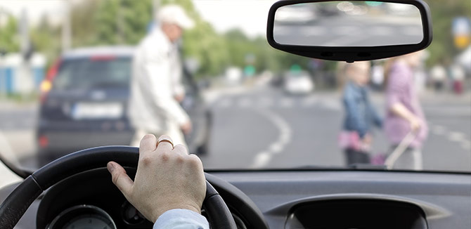 hand on the steering wheel and blurred image of people crossing the street in the windsheild